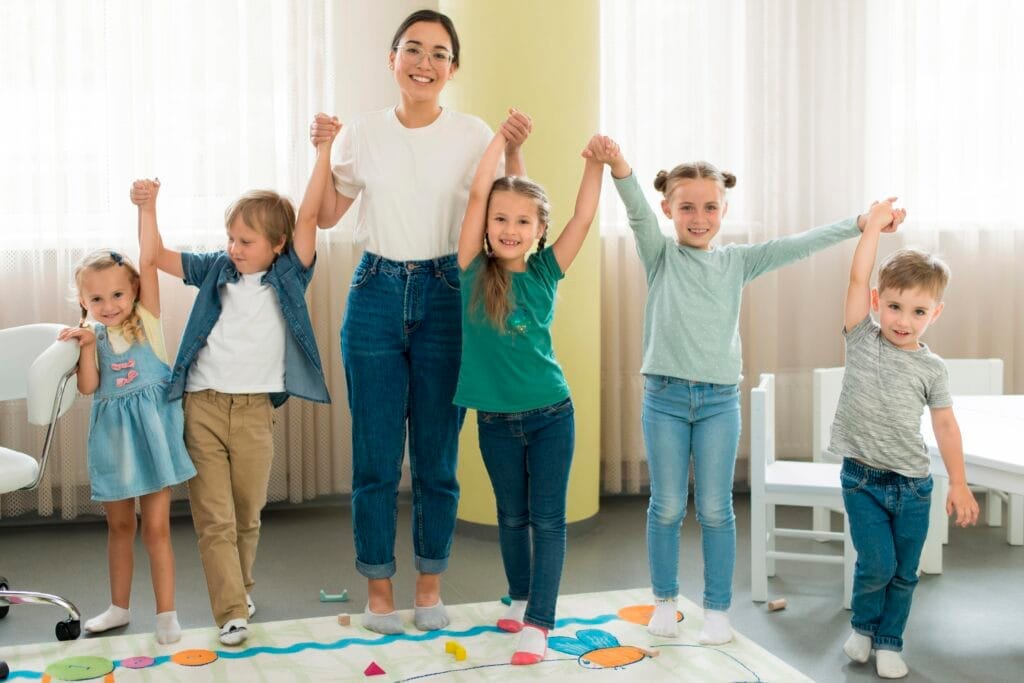front view teacher kids posing together 1 Anaokulu Kreş Öğretmenliği Kursu