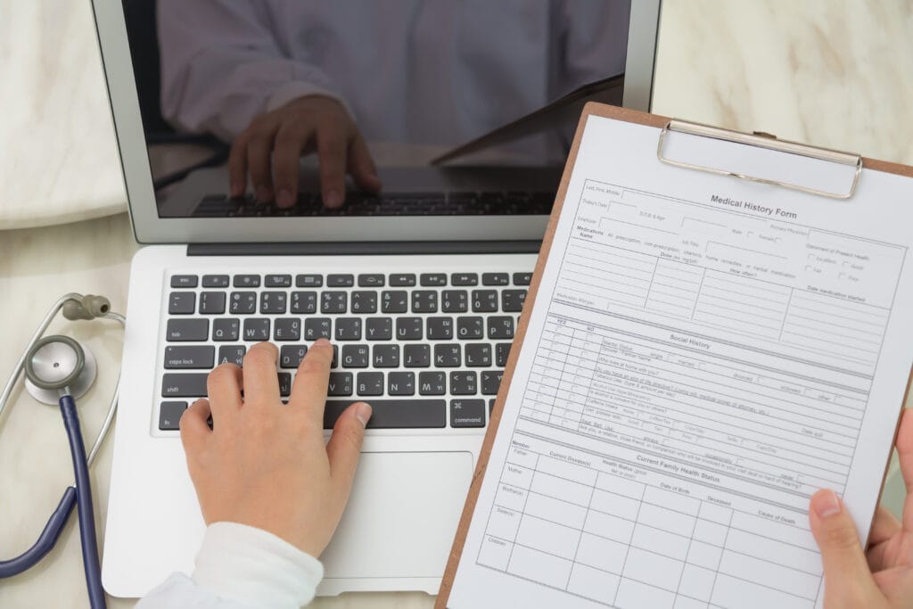 top view doctor using laptop clipboard Hasta Kabul Sertifikası Nereden Alınır