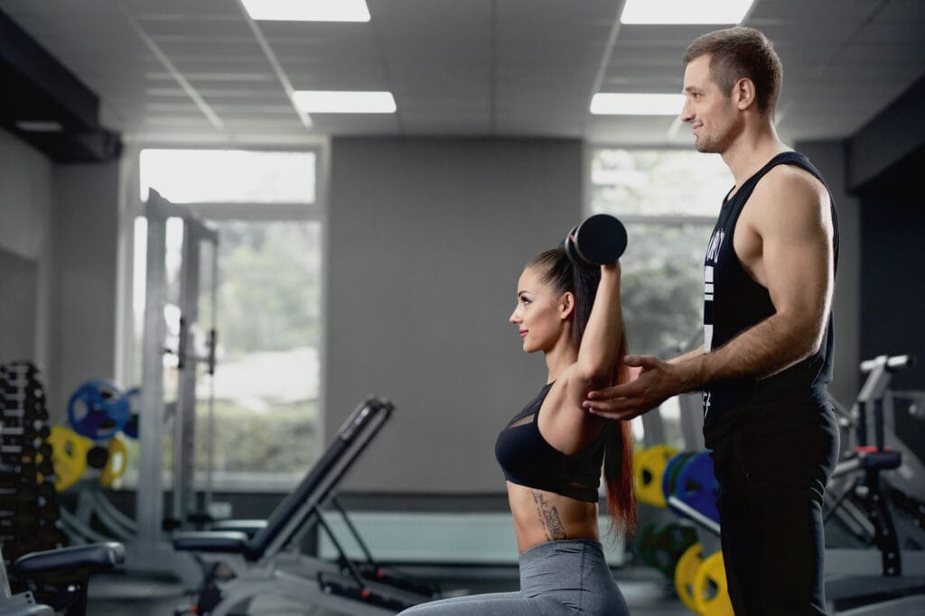male personal trainer helping woman working with heavy dumbbells gym Personal Trainer Nedir