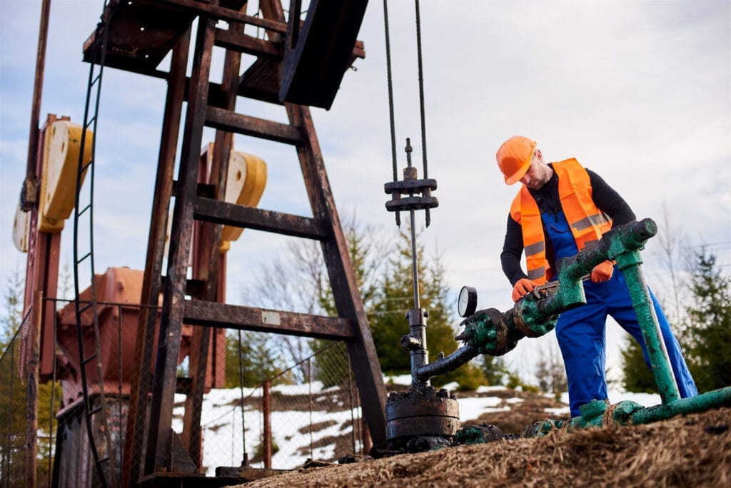 oil worker orange uniform helmet working with pipe wrench near oil pump jack Zemin Delgi Operatörlük Belgesi