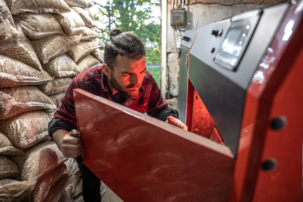 young man looking into solid fuel boiler working with biofuels economical heating Kaloriferci Sertifikası Nasıl Alınır